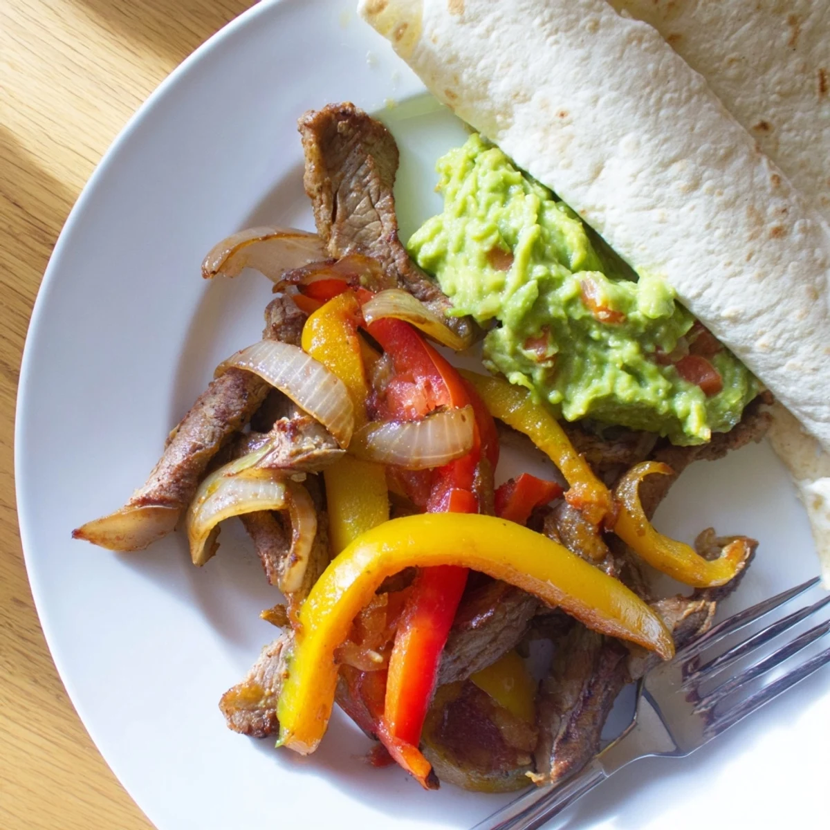 Golden-brown seared Beef Fajitas with Guacamole are plated alongside lime wedges and fresh cilantro for a festive Tex-Mex dinner.