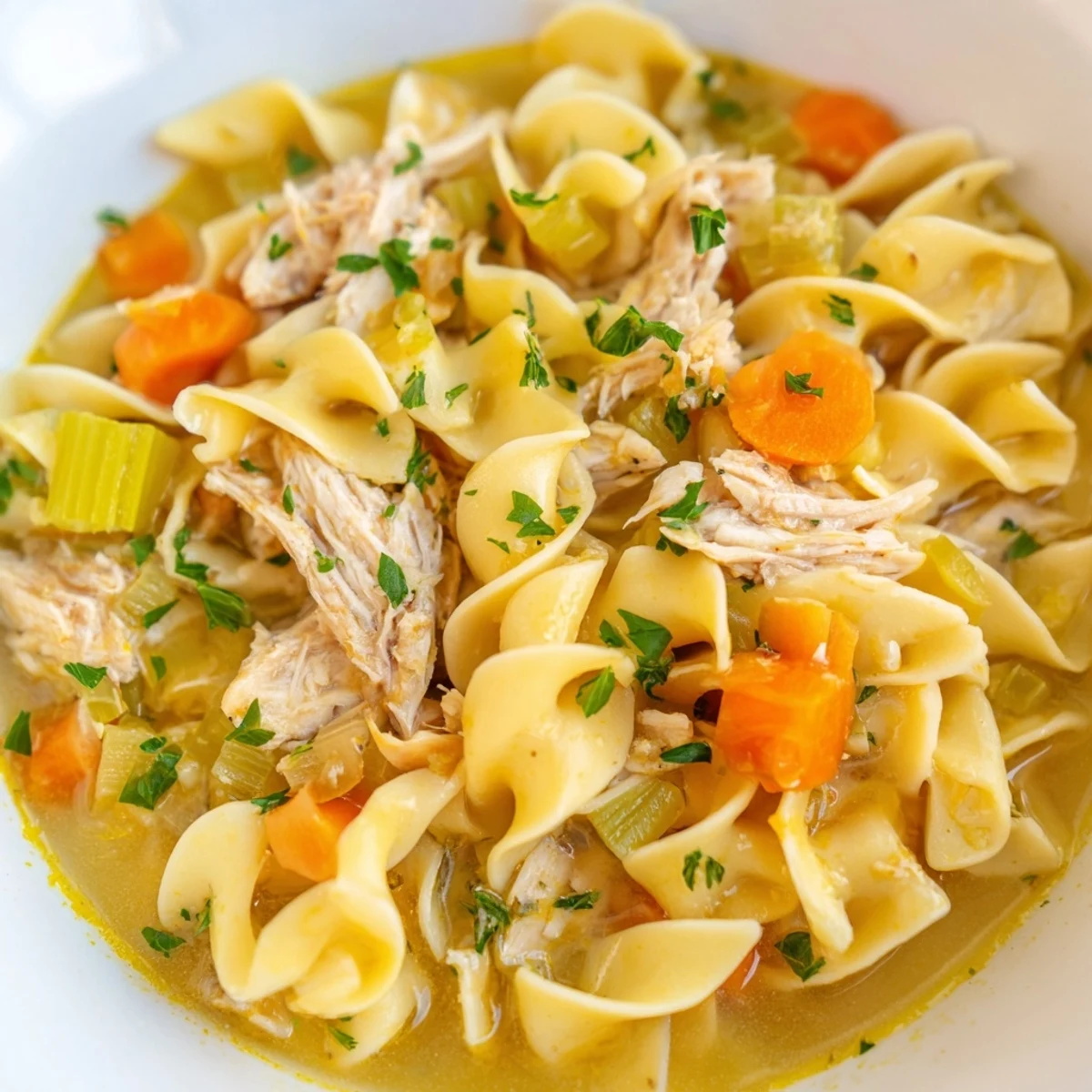 Golden egg noodles and tender shredded chicken swim in a steaming, savory broth with colorful carrots and celery.  