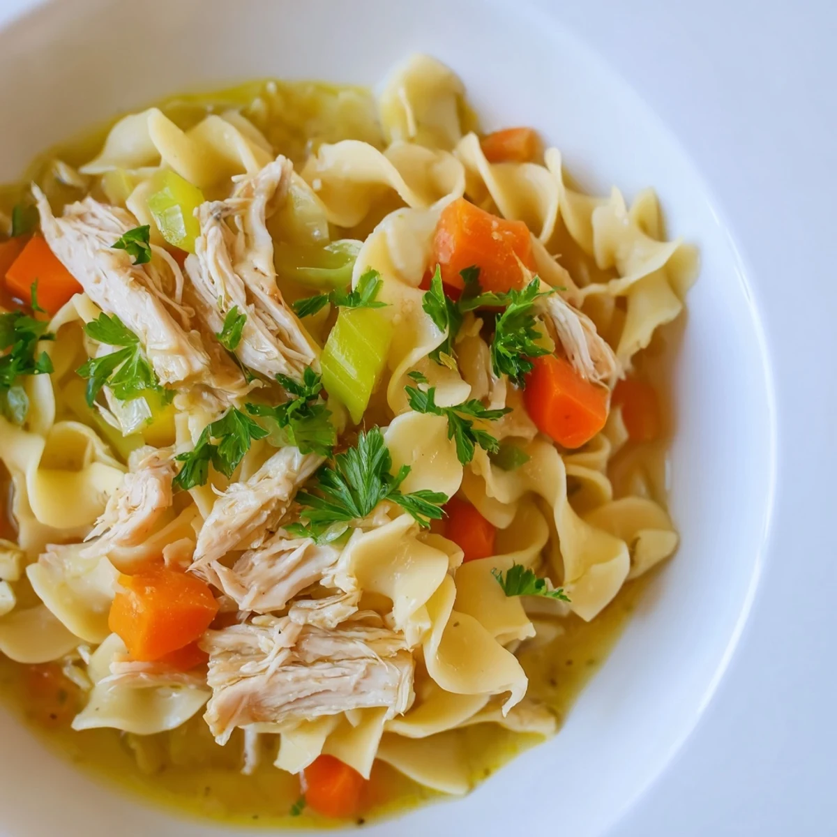 Hearty chicken noodle soup with egg noodles garnished with fresh parsley, ready to warm up chilly evenings.  