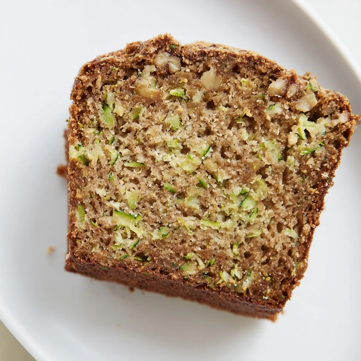 Freshly baked green zucchini bread with a moist crumb, warm cinnamon aroma, and golden-brown crust on a rustic table.  