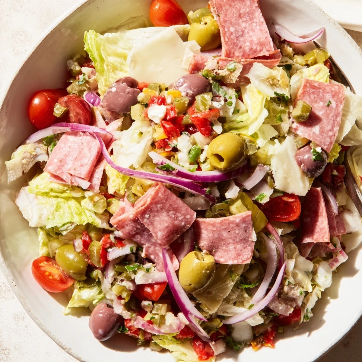 A vibrant serving of New Orleans Muffuletta Salad drizzled with garlic oregano dressing, perfect with crusty Italian bread for a zesty lunch.