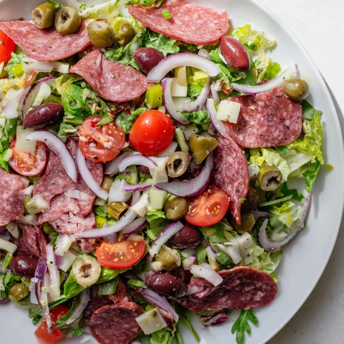 A vibrant New Orleans Muffuletta Salad topped with colorful olives, cured meats, and creamy cheese cubes.