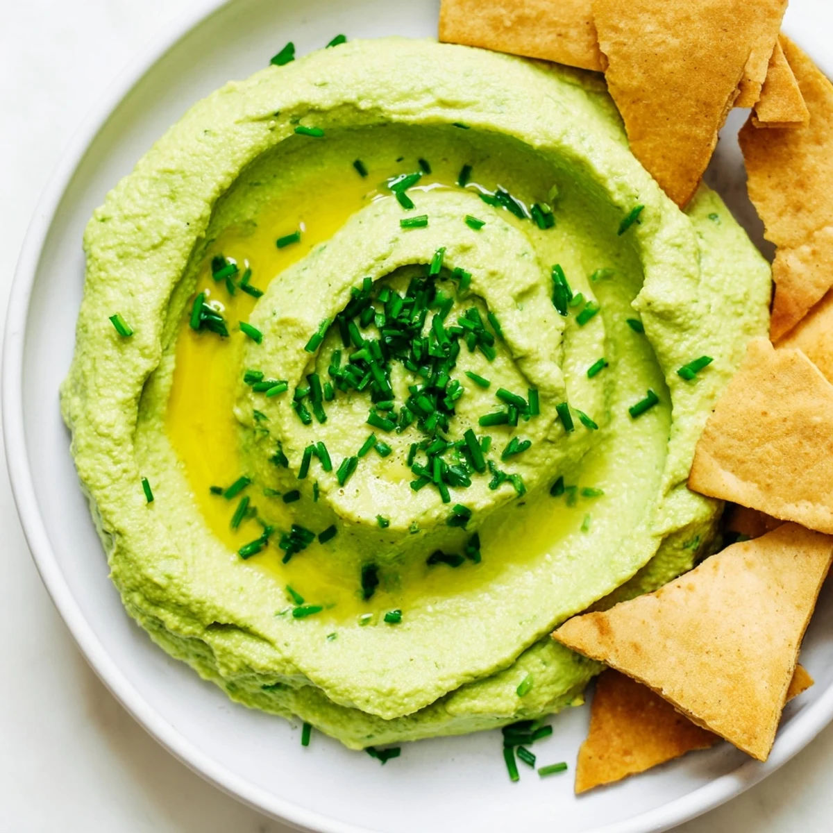 This vibrant green avocado hummus is served with crunchy homemade pita chips for a perfect snack.