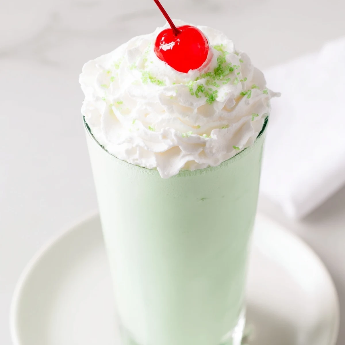 Two tall glasses of refreshing Homemade Copycat Shamrock Shake beside vanilla ice cream scoops and peppermint extract for a St. Patrick's Day celebration.