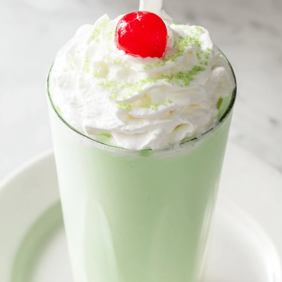 Close-up of creamy green Homemade Copycat Shamrock Shake in a tall glass, showing thick texture, minty aroma, and a sprinkle of green sugar.