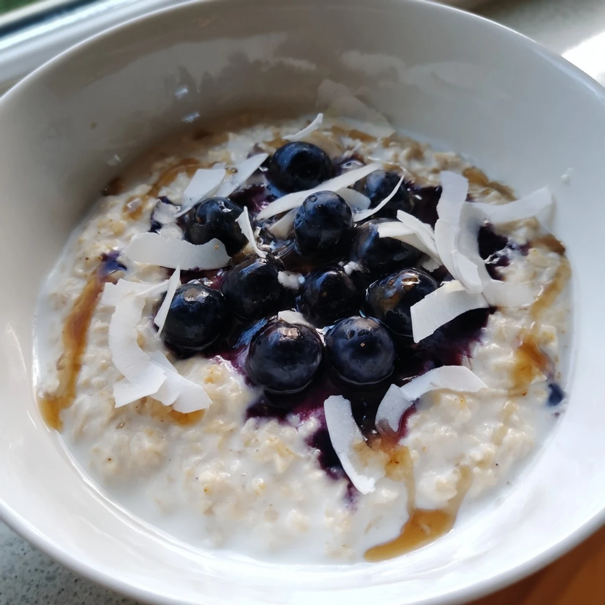A warm bowl of Tasty Coconut Cream Oats topped with fresh blueberries and toasted flakes.