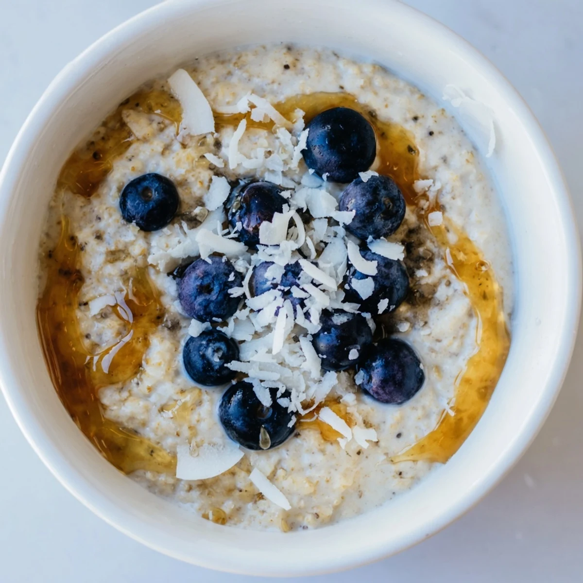 In a ceramic bowl, Tasty Coconut Cream Oats sit beside a spoon and maple drizzle.