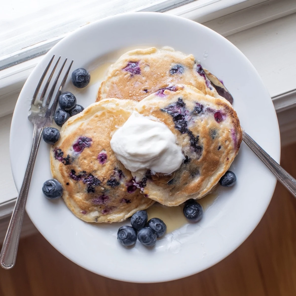 Fresh blueberries bursting inside tender Greek yogurt blueberry pancakes on a white plate