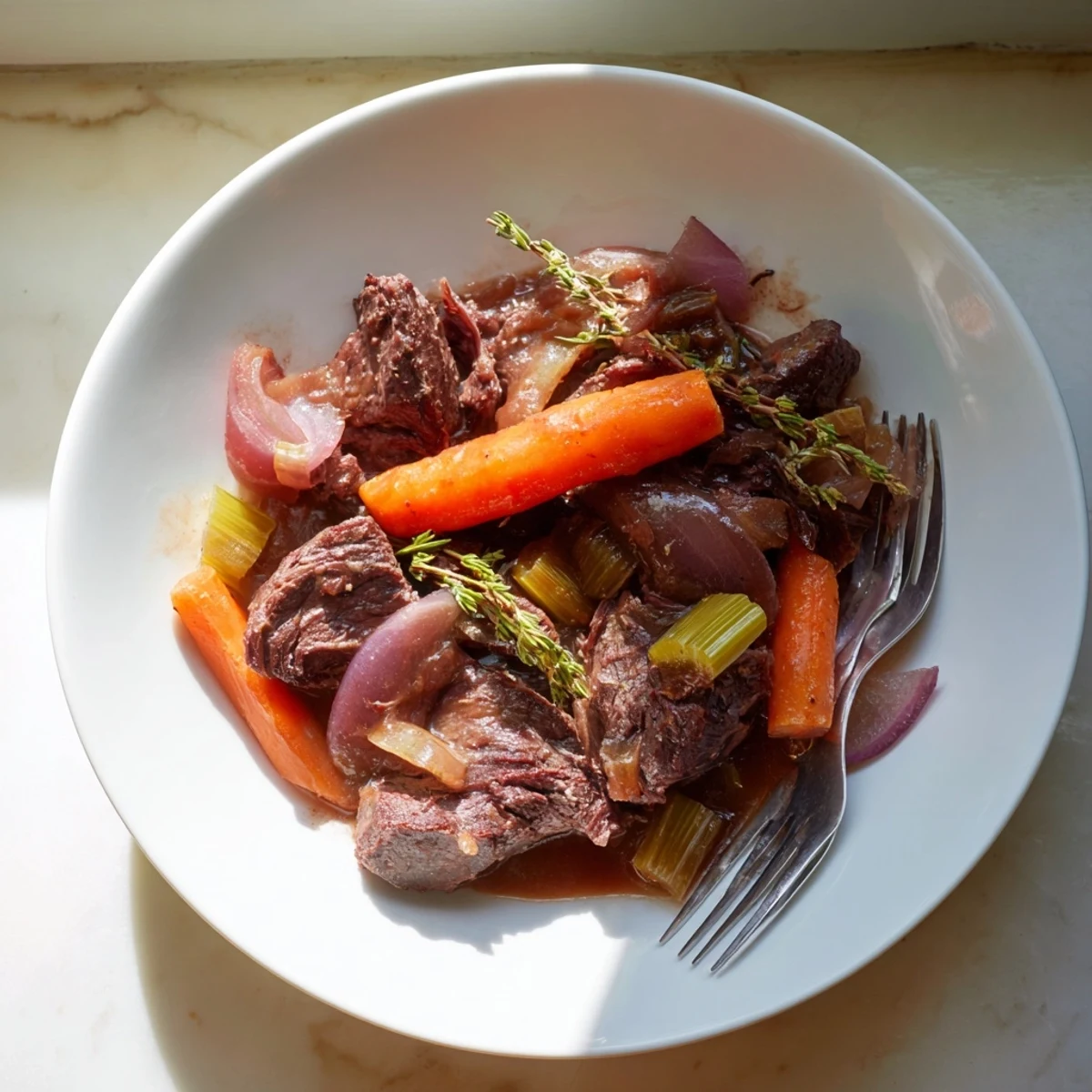 Succulent melt in your mouth red grape juice braised chuck roast sliced on a white platter garnished with fresh rosemary