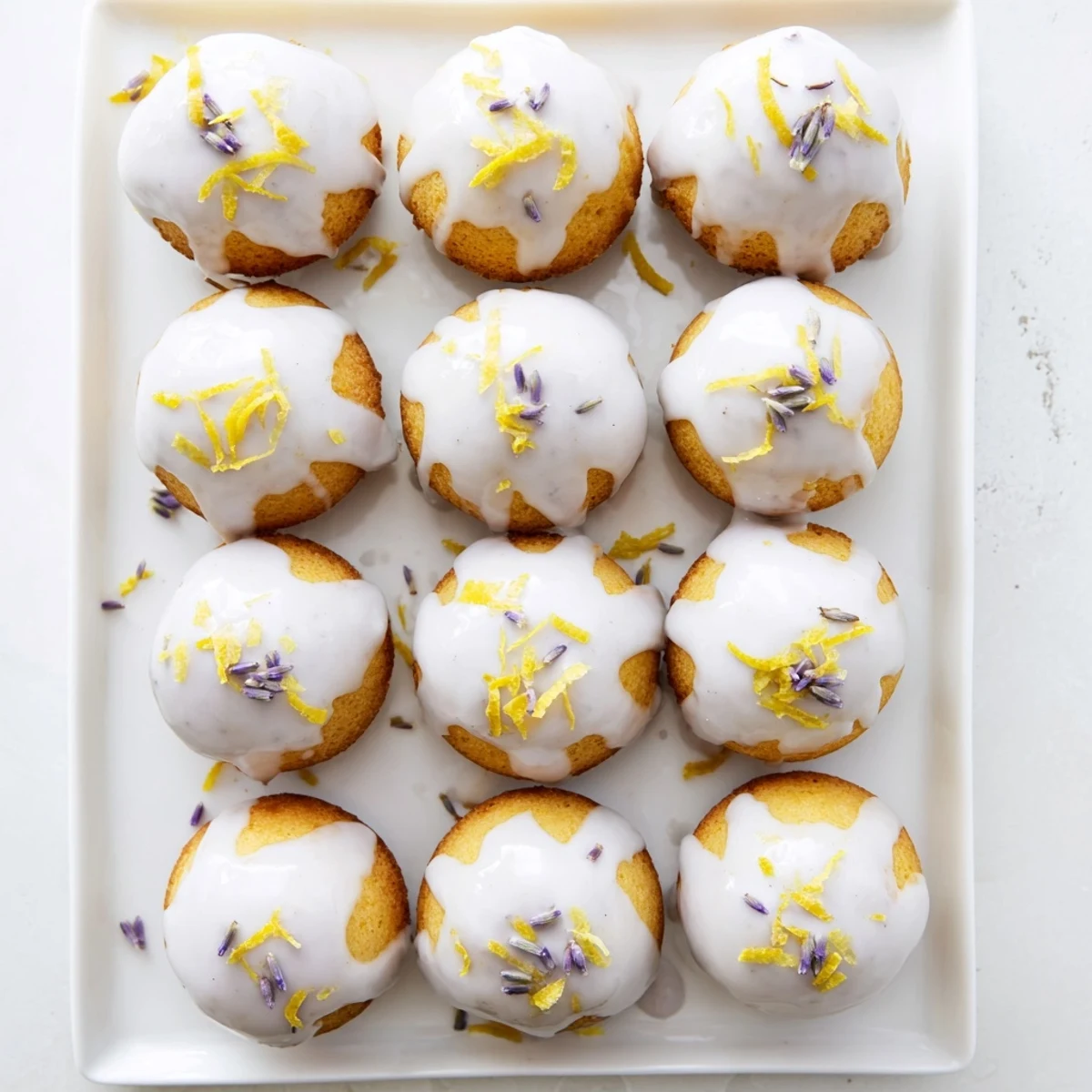 Floral lavender glazed lemon mini cakes arranged on a serving plate with scattered buds