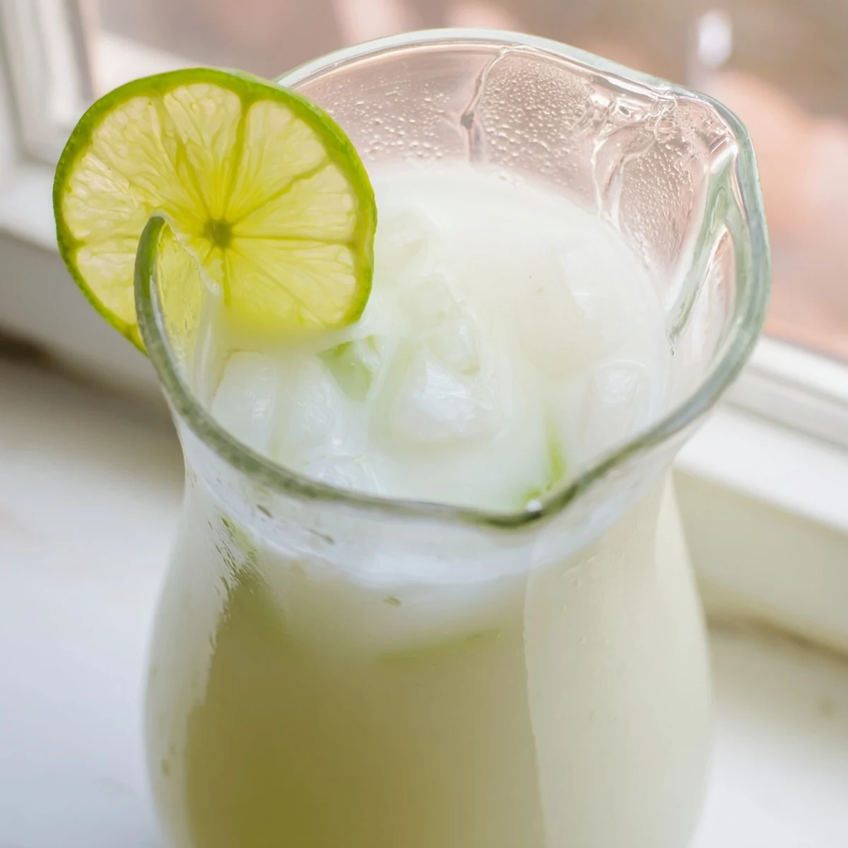 Creamy Brazilian lemonade poured over ice cubes with a wedge of fresh lime on the rim