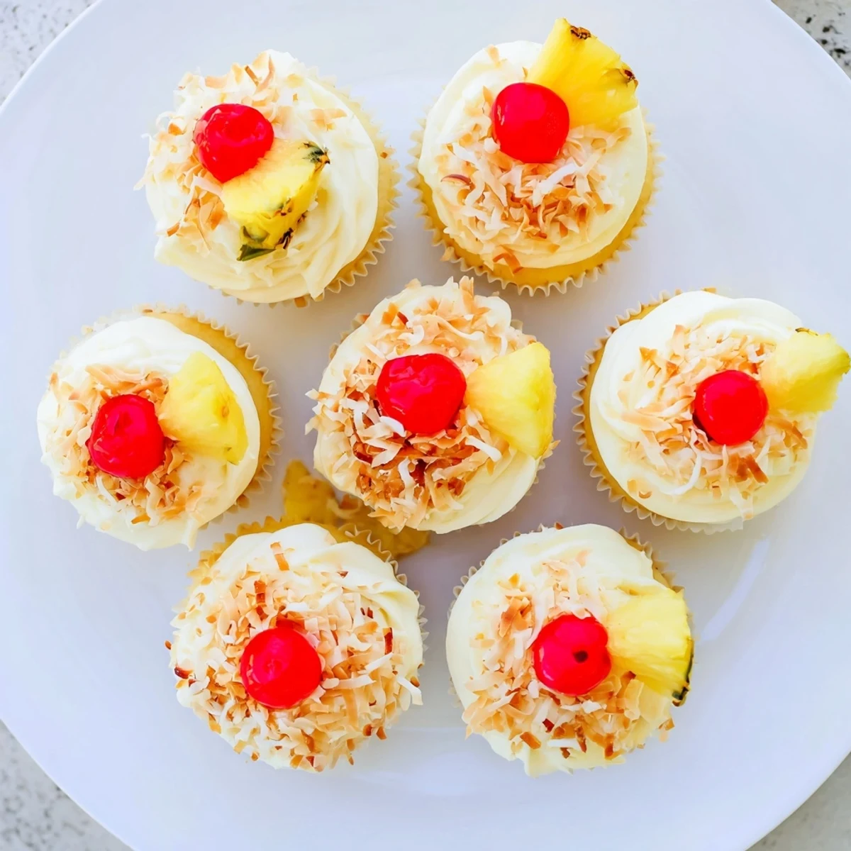 Frosted Piña Colada cupcakes topped with toasted coconut flakes and bright red maraschino cherry