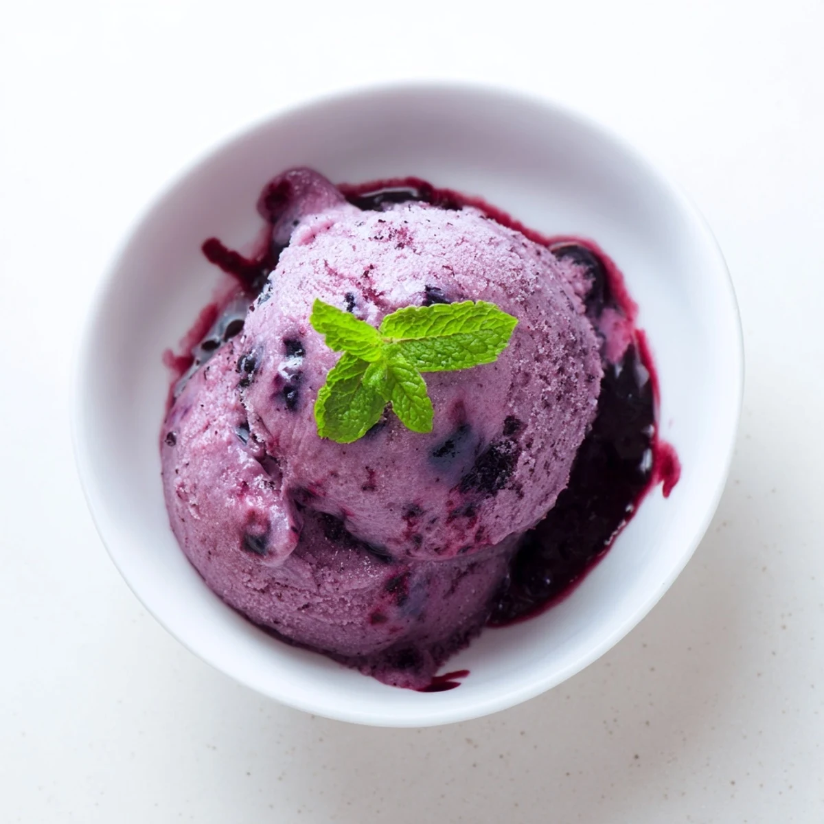 Refreshing scoop of homemade no churn blueberry lemon sorbet melting on a white plate