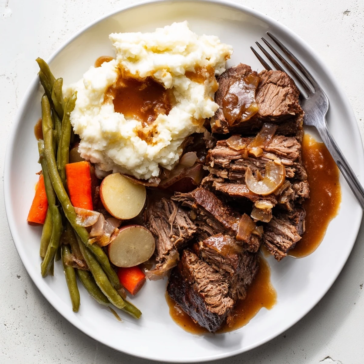 Fork-tender Southern style pot roast plated alongside buttery mashed potatoes and seasoned fresh green beans