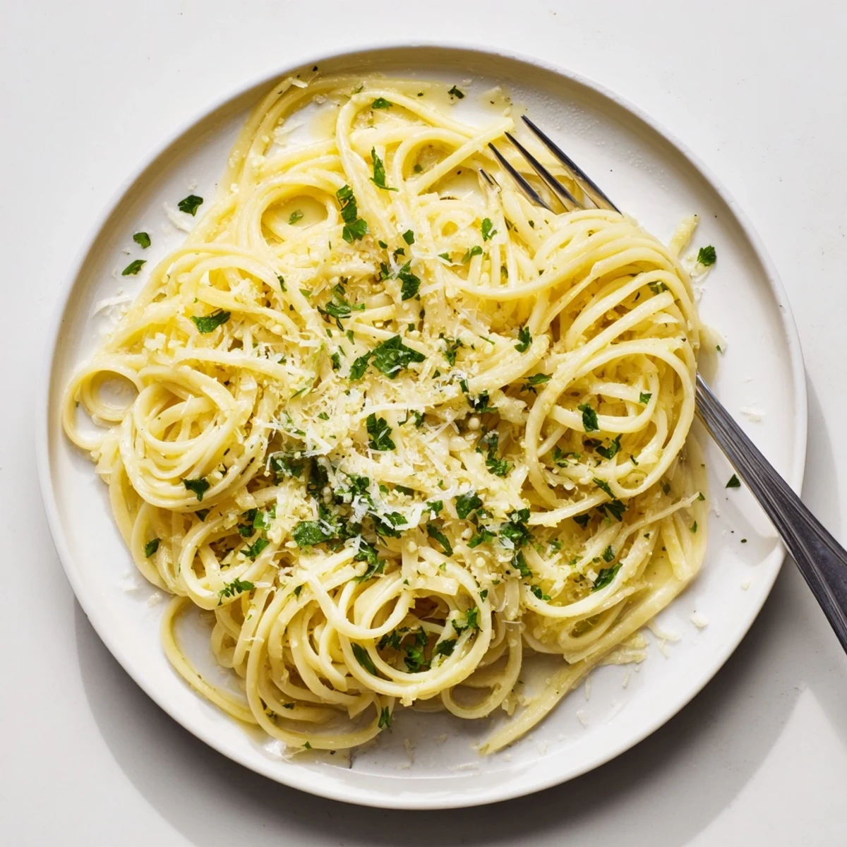 Steaming plate of garlic butter pasta coated in lemon butter with parmesan cheese sprinkles