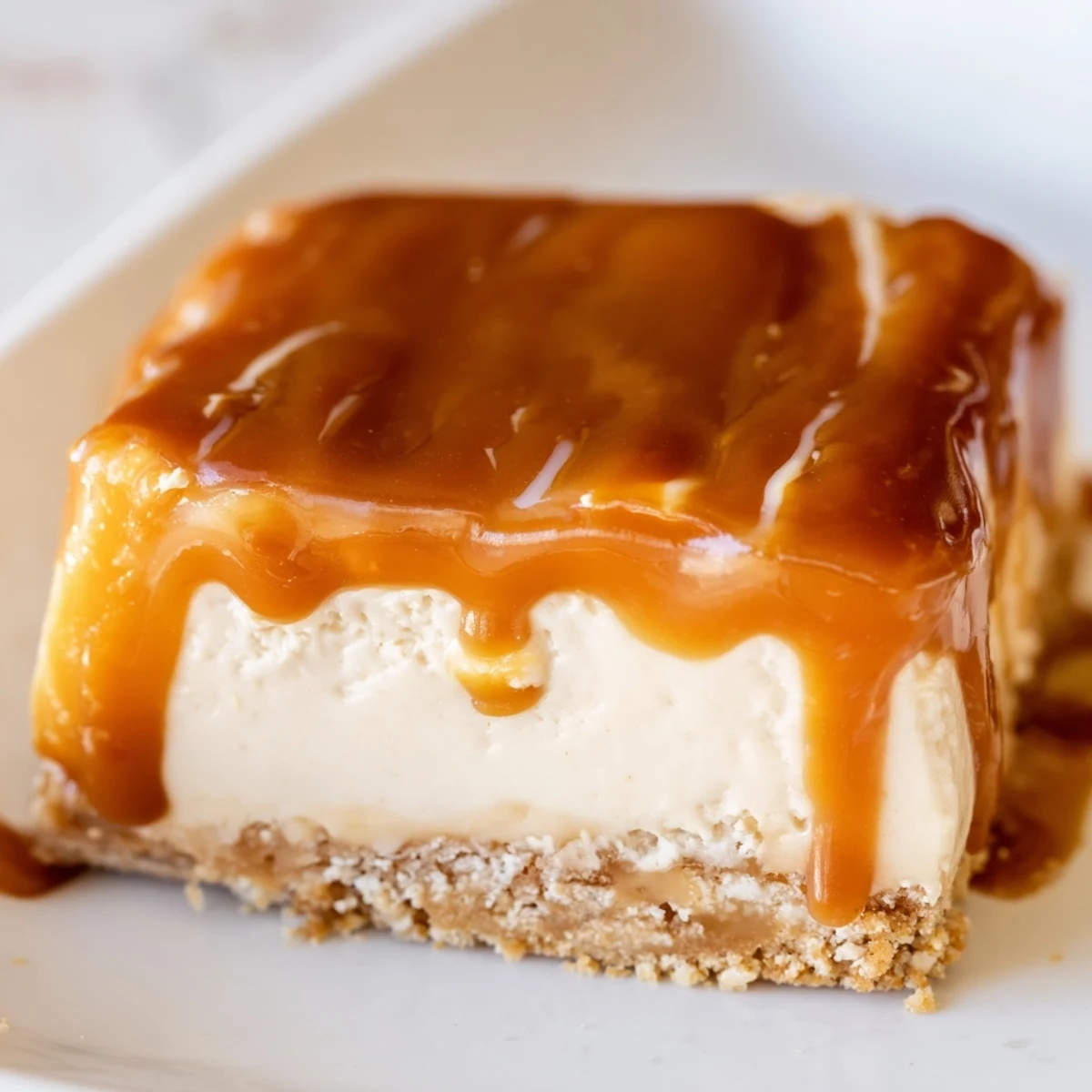 Golden caramel sauce drips down the sides of rich creamy caramel cheesecake bars on a white plate