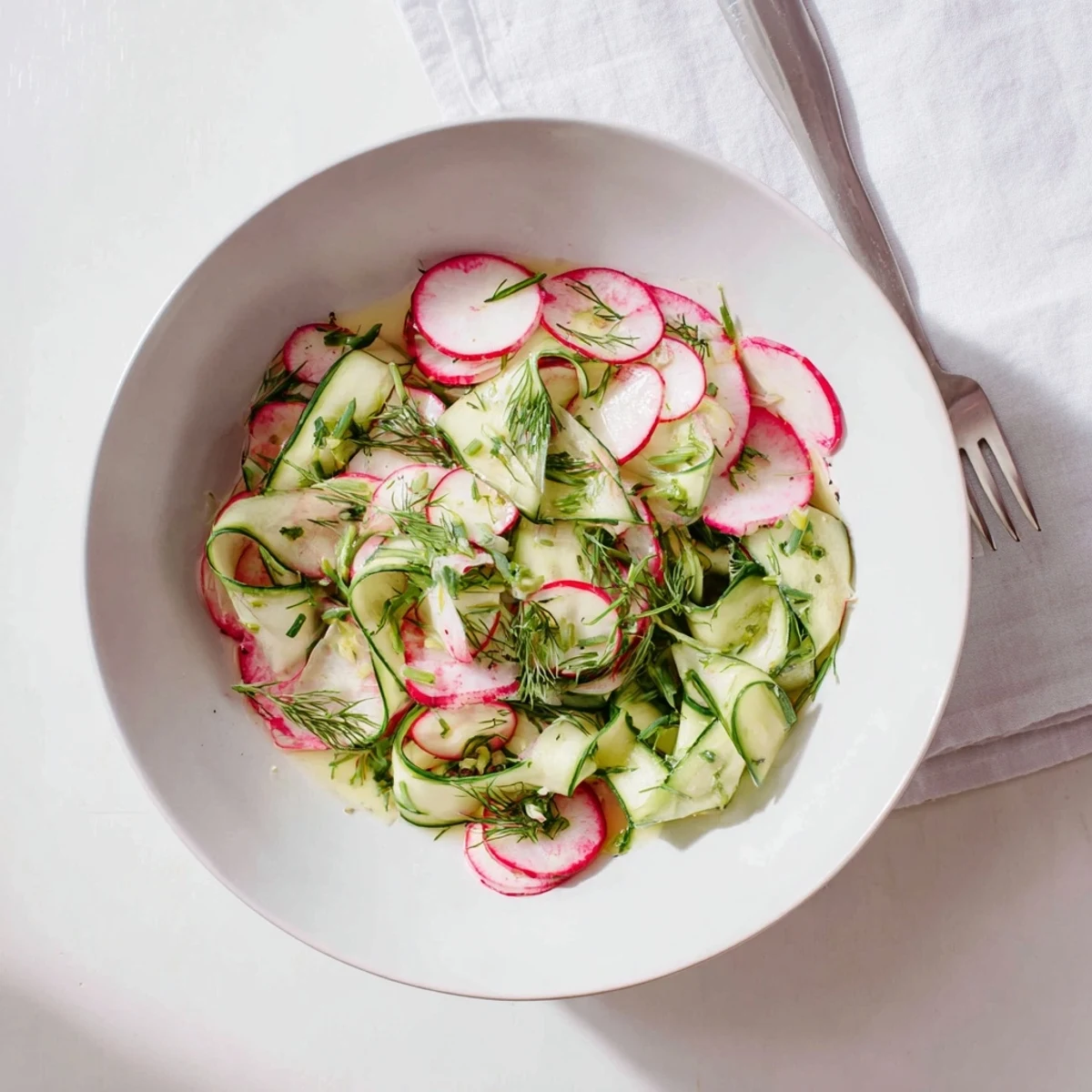 Fresh radish and cucumber salad arranged in a white serving bowl with bright green dill garnish