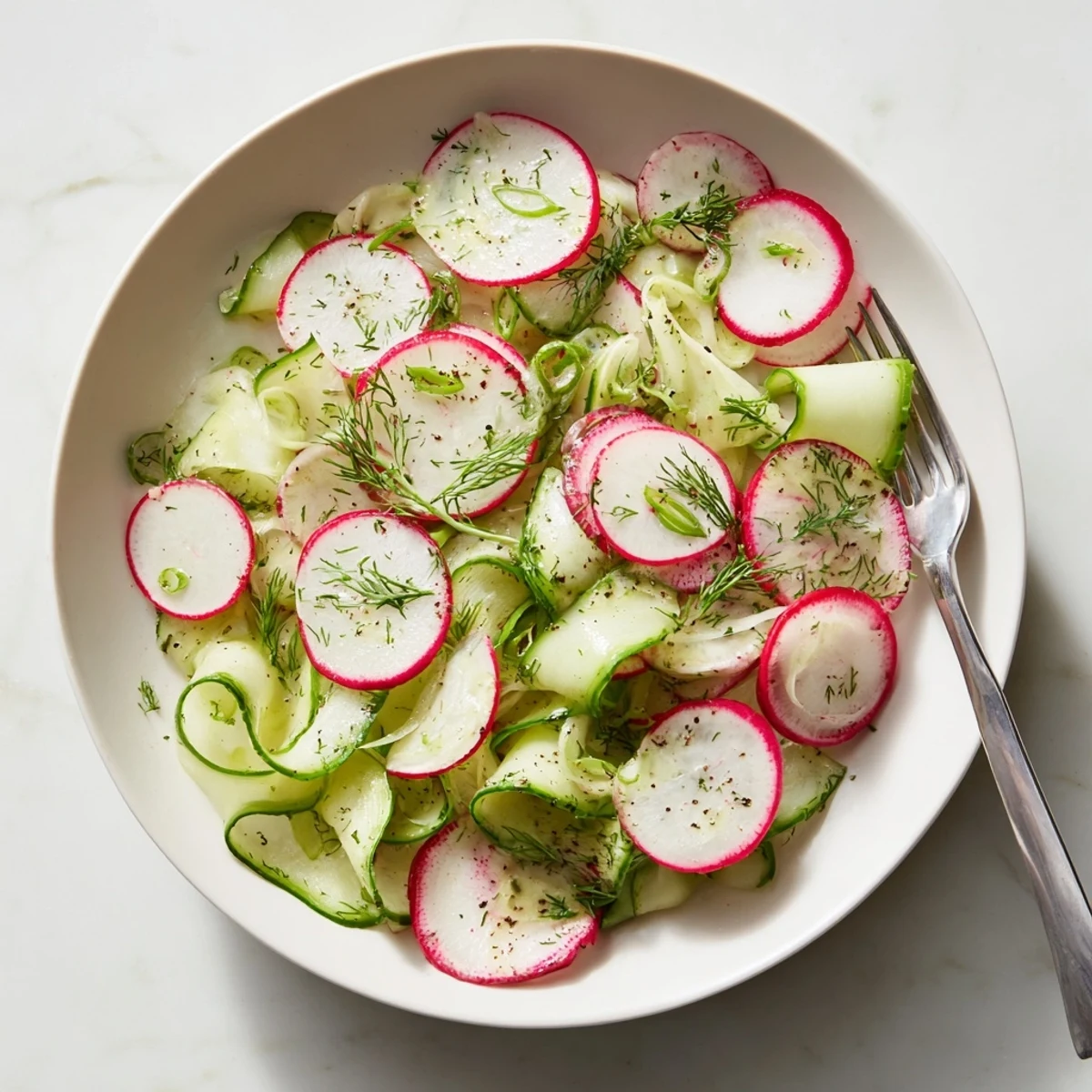 Colorful radish and cucumber salad features thinly sliced vegetables drizzled with olive oil and fresh herbs
