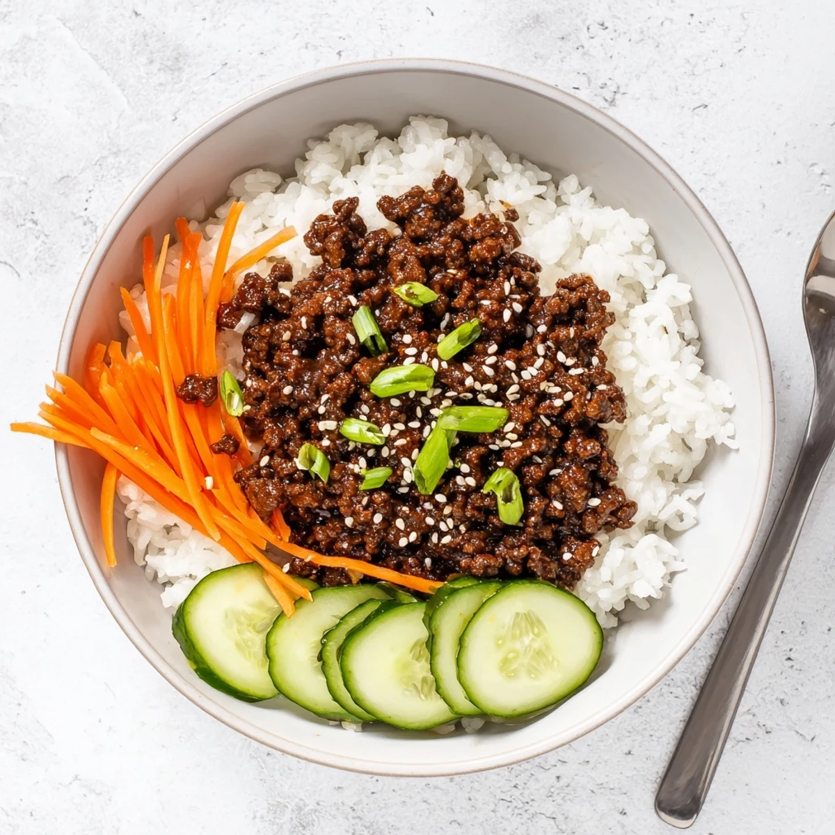 Korean beef bowls featuring caramelized ground beef, crisp cucumber, and julienned carrots over steamed rice
