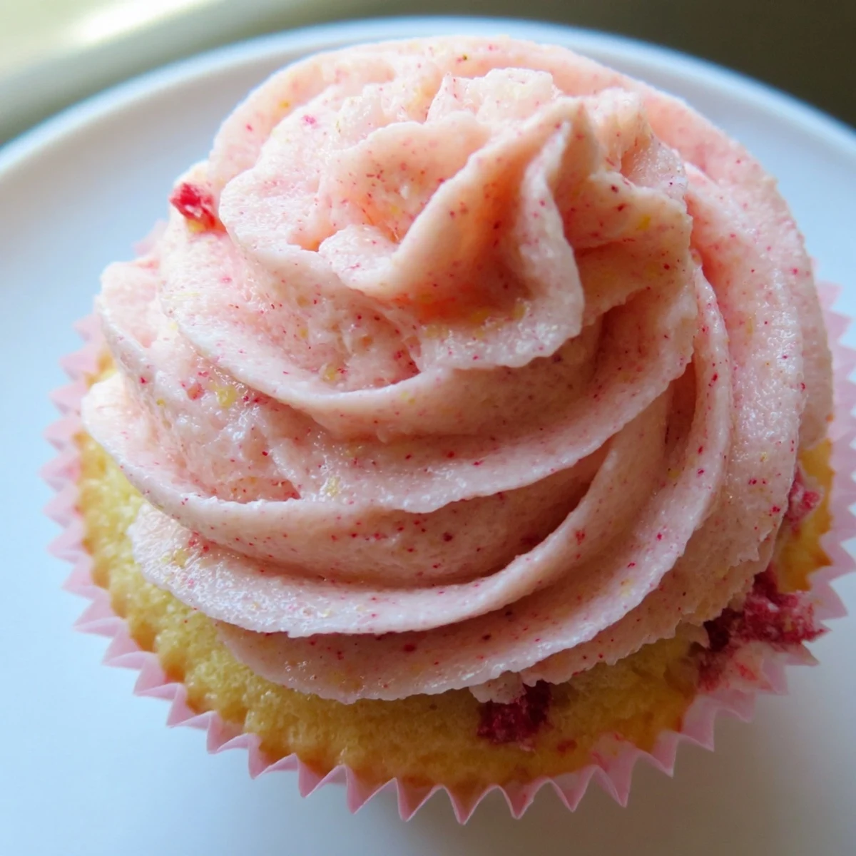 Frosted strawberry lemonade cupcakes topped with pink buttercream on a rustic summer table