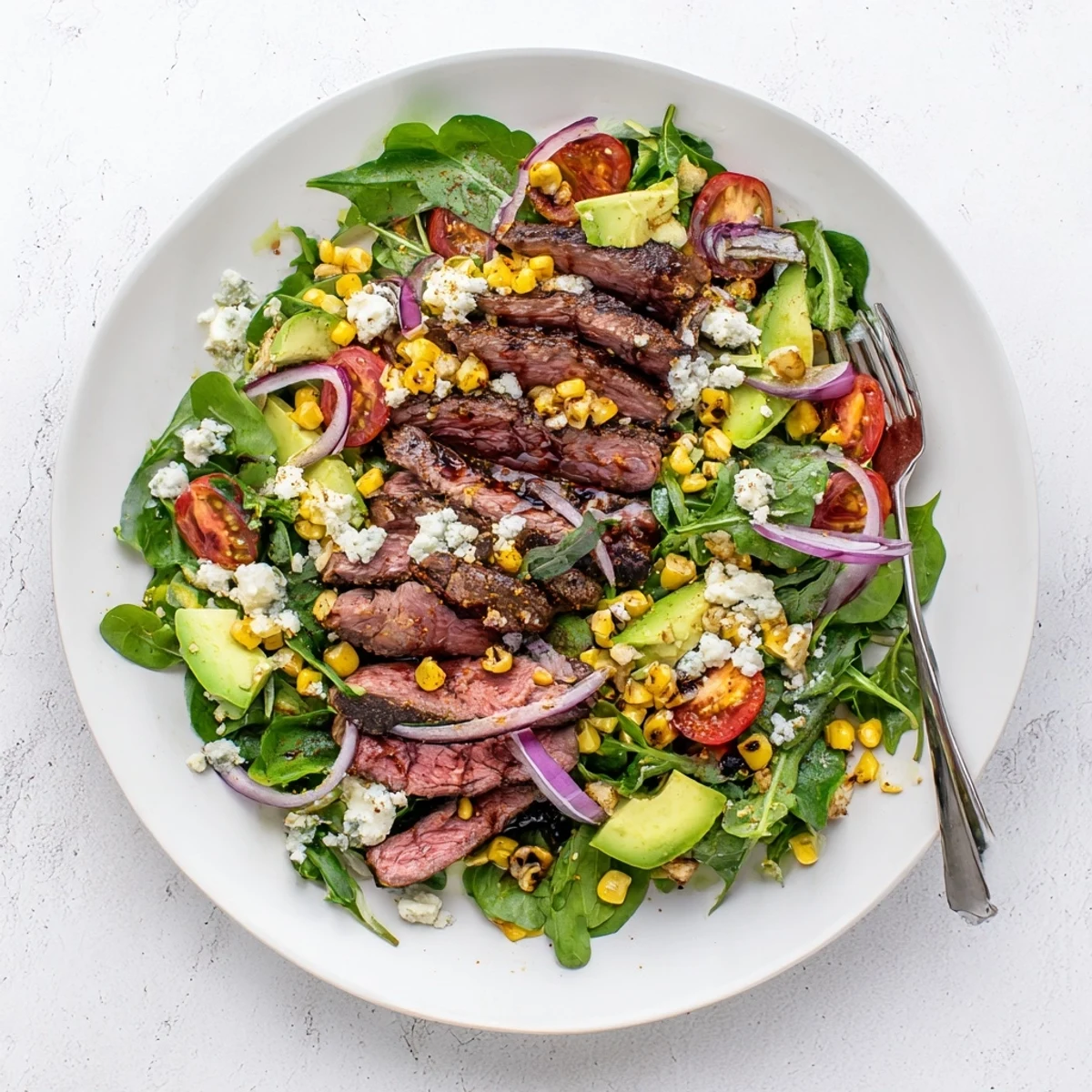 Sliced balsamic steak draped over crisp greens with charred grilled corn and crumbled Gorgonzola in a balsamic steak Gorgonzola salad with grilled corn