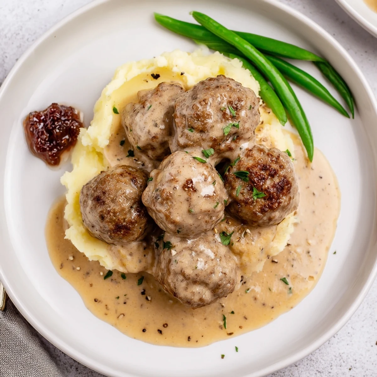 Homemade Ikea Meatballs glazed in creamy gravy, steaming over mashed potatoes