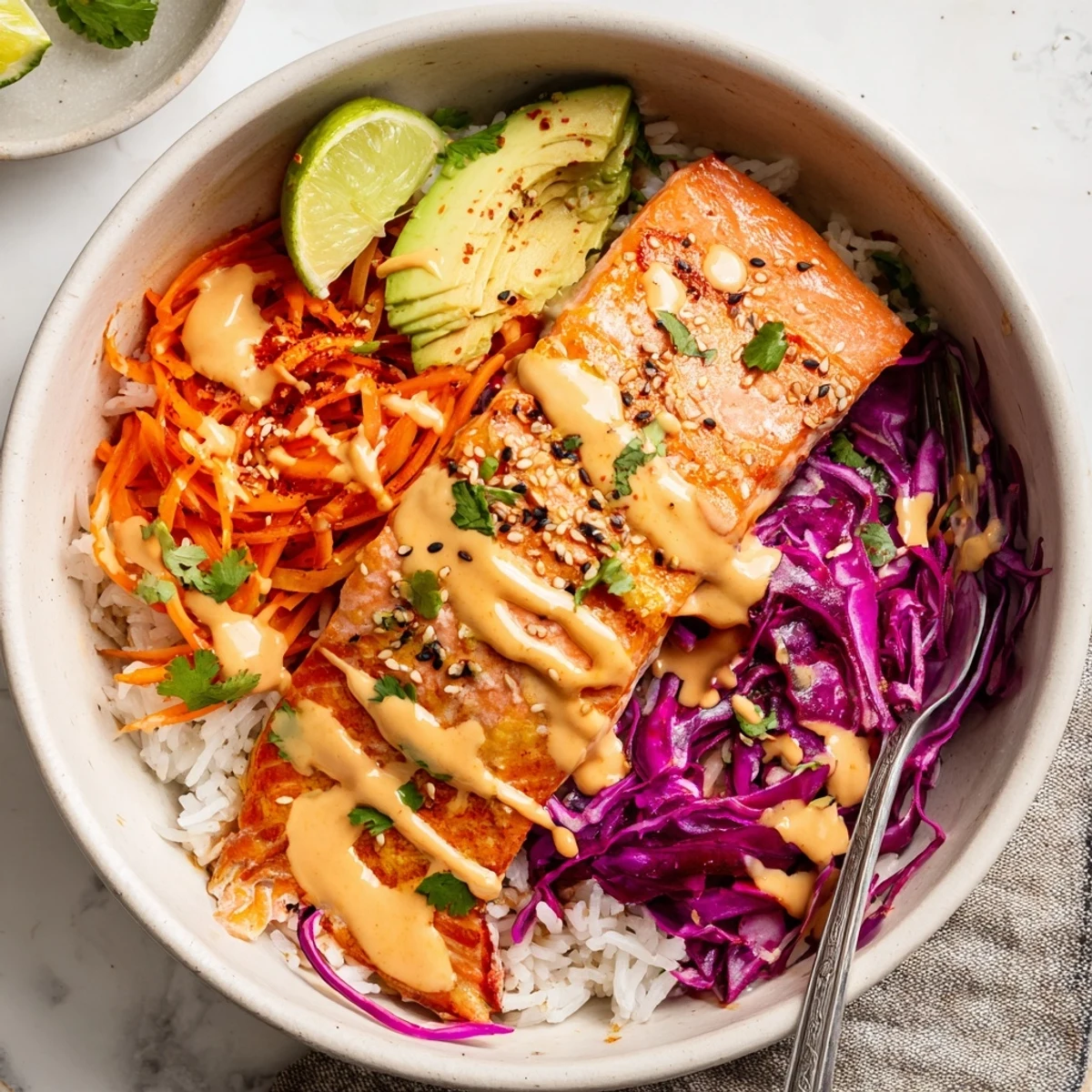 Savory Bang Bang Salmon Bowls Recipe served over fluffy jasmine rice, lime wedges