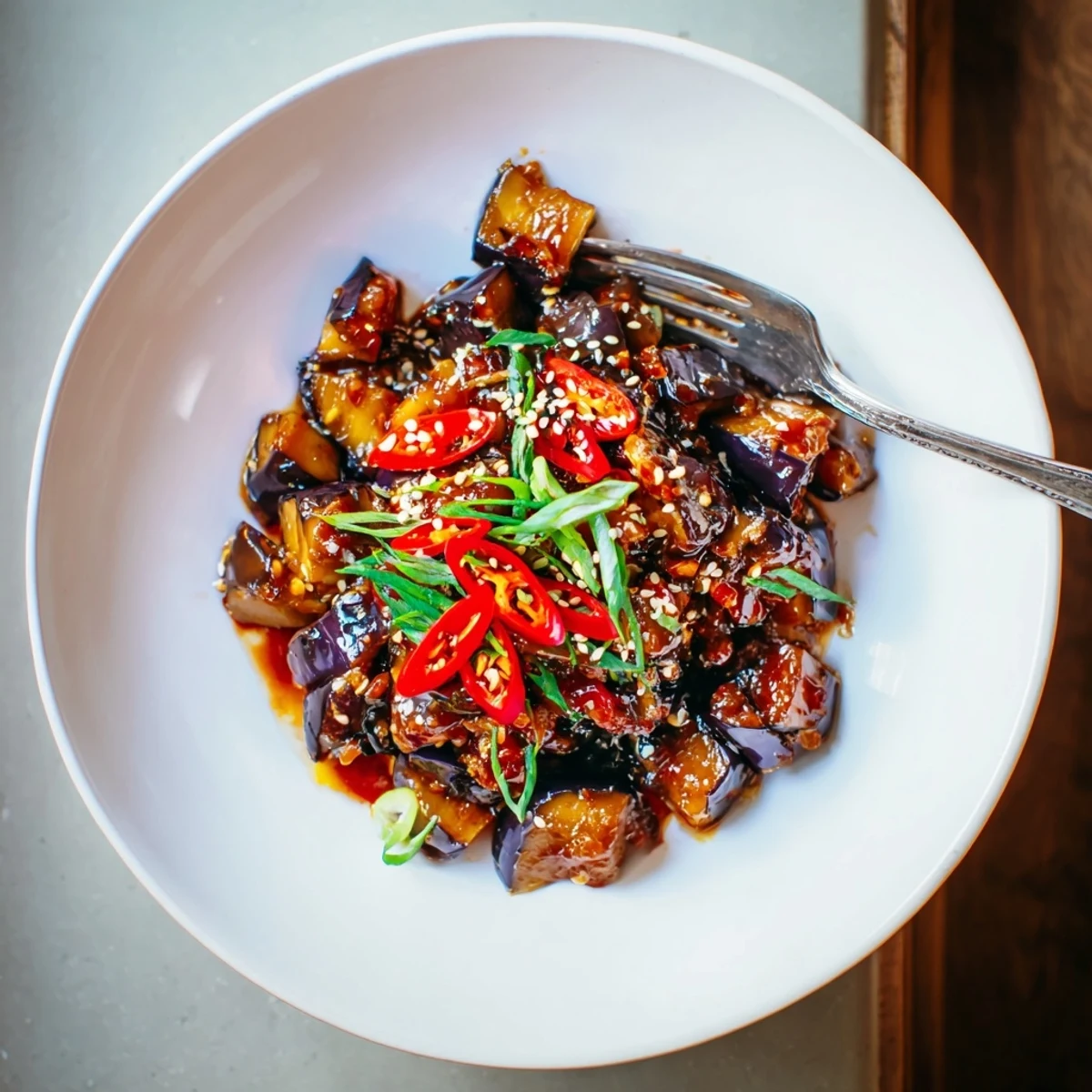 Sichuan Style Braised Aubergines glistening in spicy sauce, topped with sliced scallions