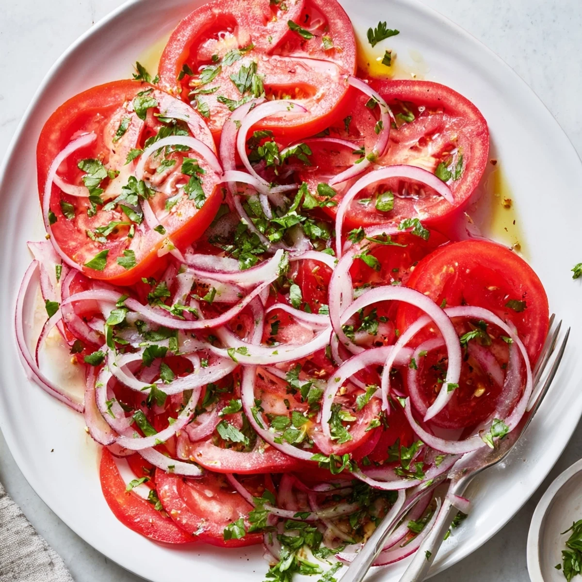 Sliced red onions and ripe tomatoes arranged in a colorful layered salad with light dressing and fresh green herbs