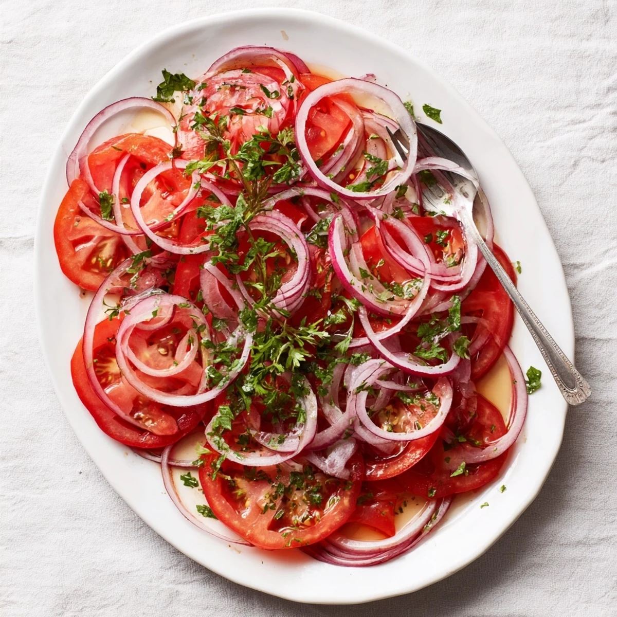 Fresh tomato and onion salad drizzled with olive oil vinaigrette and garnished with parsley on a white serving plate