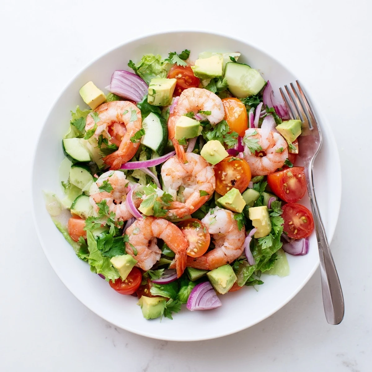 Colorful shrimp avocado salad recipe arranged in a bowl with cherry tomatoes, crisp cucumber, red onion, and leafy greens tossed in lime olive oil