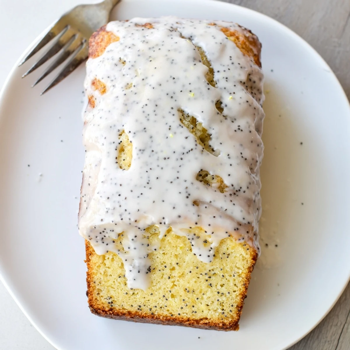 Golden lemon poppy seed loaf cake drizzled with white glaze on a white plate