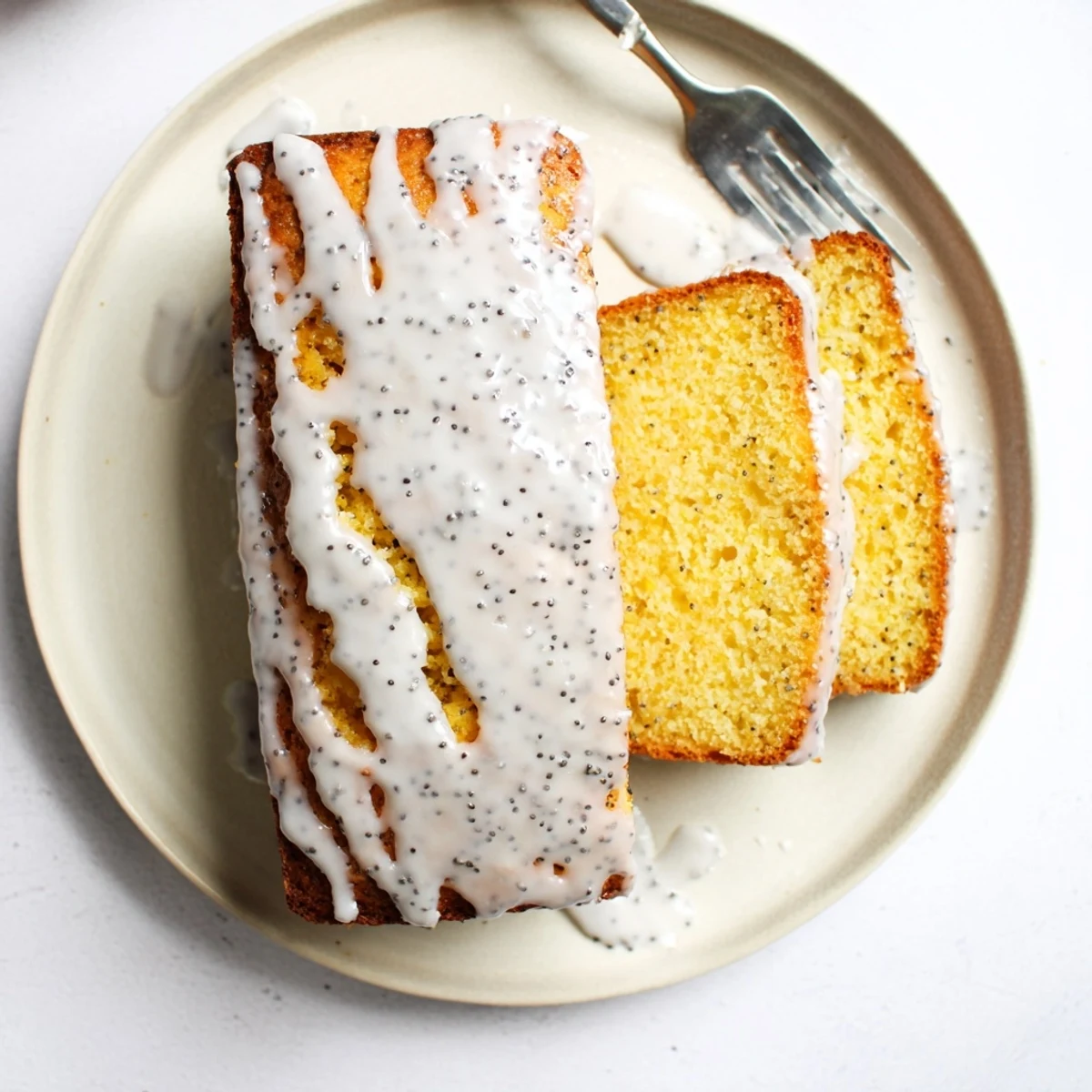 Moist lemon poppy seed cake slice with dotted interior and sweet lemon icing topping