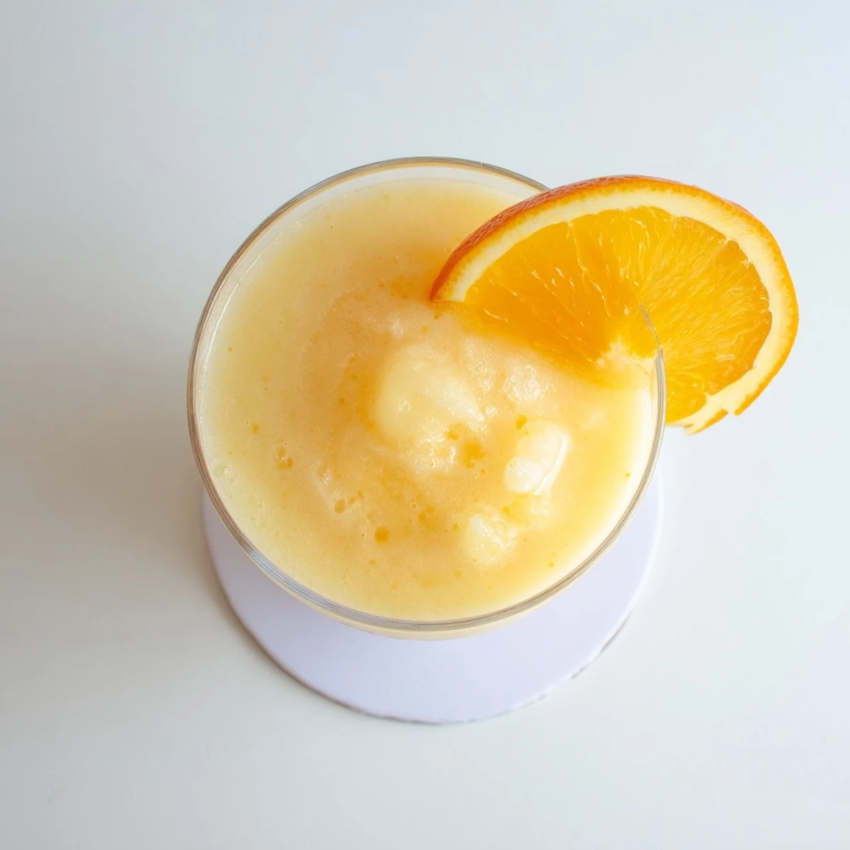 Tall chilled glass filled with creamy orange slush displaying smooth icy consistency and topped with zesty orange garnish.
