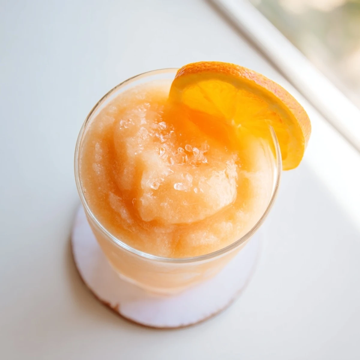 Close-up of swirled frozen orange cream slush highlighting the vibrant orange hue and creamy vanilla finish in a frosty glass.