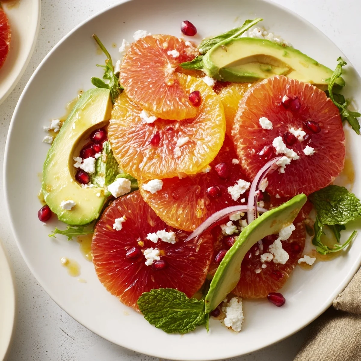 Colorful citrus salad with pomegranate seeds, creamy avocado slices, and crumbled feta on a platter