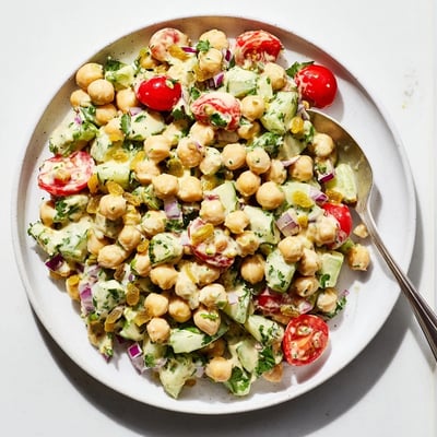A close-up view of creamy Curried Chickpea Salad showing tender chickpeas, diced cucumbers, and golden raisins mixed with curry dressing.