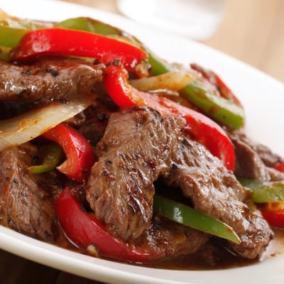 Close-up of Sizzling Chinese Pepper Steak With Onions plated with fluffy rice, garnished with fresh scallions and sesame seeds.