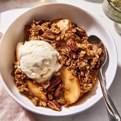 Crockpot apple crisp served in a bowl with melting vanilla bean ice cream